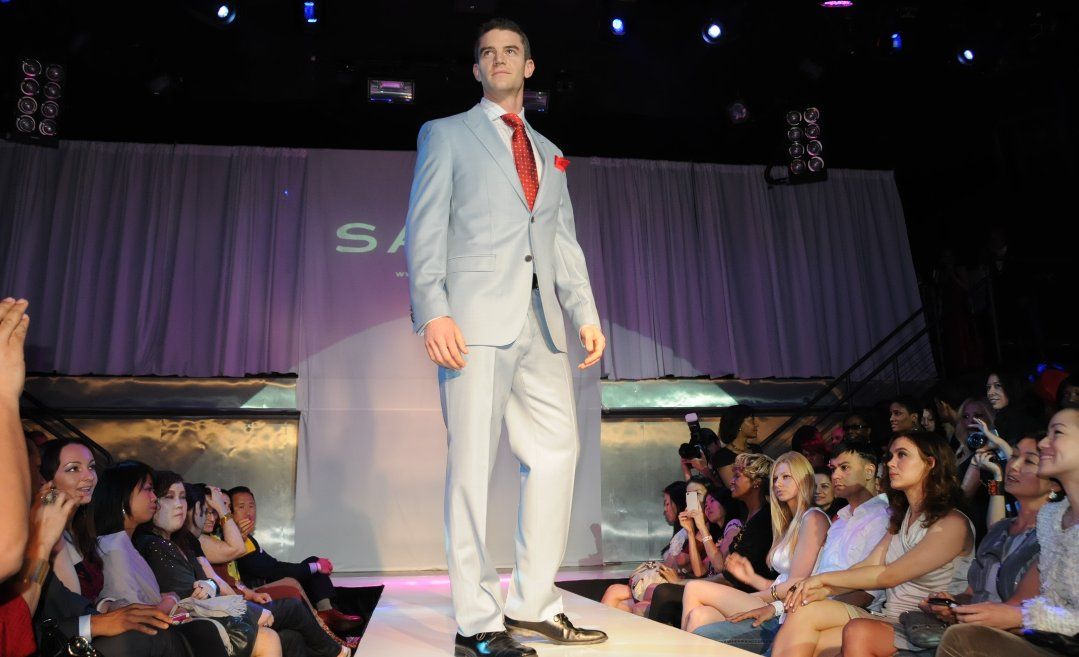 Male fit model Joe Cummings walking a runway in a light blue suit with a red tie